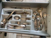 Drawer view showing silver plate cutlery in two trays with forks, spoons, specialty knives, and serving forks of different styles.