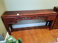 View of full wooden console table placed against a green wall with two drawers and visible wood grain and scratches on top surface