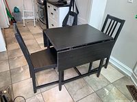 Black painted wood IKEA kitchen table with two matching chairs; table shown partially open with foldout extensions.
