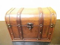 Front profile of vintage wooden box with leather straps and metal rivets, showing latch and scratches.