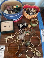 Top view of two decorative boxes containing assorted jewelry including watches, pins, bracelets, and earrings spread on a table.