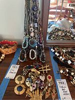 Assorted costume jewelry laid out on a table including bracelets, pins, and necklaces with offering tags