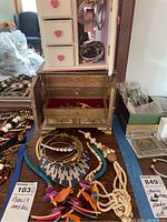 Full view of jewelry lot with multiple necklaces and bracelets arranged on table and small wooden jewelry chest with drawers containing additional jewelry items.