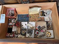Top view showing multiple small boxes and loose costume jewelry pieces including earrings, bracelets, and necklaces inside a drawer.