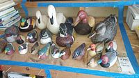 Full view of 20+ duck figurines of various sizes and styles laid out on a wooden table showing front and side profiles.