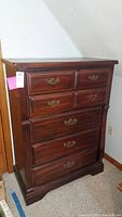 Front view of wooden highboy dresser showing five drawers and brass handles.