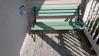 Full view of the green painted wood slat bench with black metal frame on a wooden porch floor showing weathered condition.