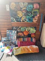 Rolled colorful pool towels stacked in two rows with beach ball and floating chair in packaging on the floor.