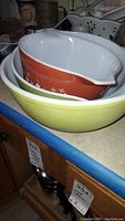 Stacked view of three Pyrex mixing bowls showing yellow, avocado, and rust exteriors with pouring spouts.
