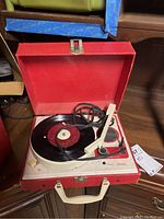 Red vintage portable record player with tonearm and record inside red carrying case.