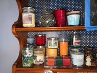 Shelf with various scented jar candles including Yankee brand and artisan candles, plus red votive glass candle holder