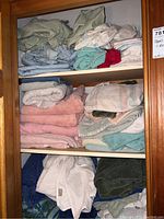 Three wooden shelves filled with assorted folded towels in various colors including pink, white, green, and blue.