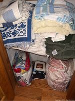 Stack of mixed towels and bedding in blue, cream, white, and green colors showing different textures and patterns.