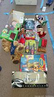 Lot of mixed toys including Sing With Me Madeline doll in box, Bionicle Inika, cheerleader nutcracker, teddy bears, walkie talkies, toy trucks and several other small toys arranged on floor.