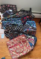 Overview photo of 11 Vera Bradley purses and bags arranged on wooden floor showing various colorful floral and paisley patterns.