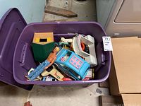 Large purple storage bin containing assorted vintage toys including plastic vehicles and a figurine.