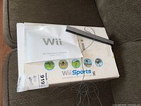 Wii Sports box with sensor bar on top and white Wii Operations Manual folded on box.
