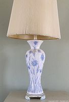 Side view of one of the matching bedside lamps showing white ceramic base with blue floral pattern and beige pleated lampshade