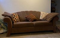 Brown cloth sofa with rolled arms and vertical tufting, several pillows on seat and arms. Sofa measures approximately 84x36x36 inches.