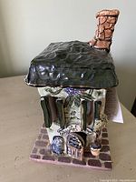 Front and side view of the ceramic cottage night light showing detailed windows, door, chimney, and textured roof.
