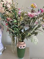 Photo of ceramic vase holding colorful artificial flowers in a variety of shapes and textures
