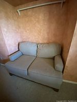 Photo of a tan cloth loveseat against a muted orange textured wall, showing overall condition and style.