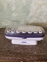 Conair Instant Heat Hairset heated curlers closed inside a clear plastic case on a brown surface.