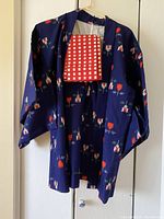 Front view of navy blue silk kimono-style jacket with floral print and red checkered sash hanging on white wall