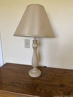 Beige table lamp with pleated fabric shade on wooden table against white wall.