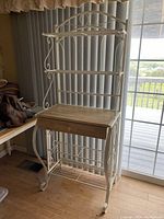 White metal and wood plant stand in room near sliding glass door, showing full height and shelves with drawer.