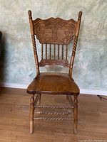 One of four solid oak dining chairs showing carved backrest with floral and scroll motifs, turned legs with spiral twist detail, and contoured seat in good condition.