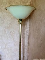Tall floor lamp with brass-colored metal stand and frosted white glass shade facing upward.
