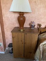 Tan ceramic lamp with pleated shade on top of wooden nightstand with other small decorative items.