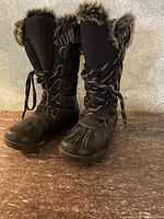 Pair of waterproof winter boots in size 7, dark brown with faux fur lining and lace-up front, placed on a wooden surface against a neutral background.