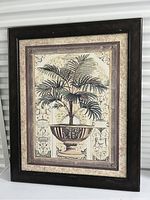 Photo of framed painting featuring a potted palm plant with decorative background and dark wooden frame.