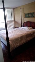 Front angled view of queen size wooden four-poster bed with carved tall posts and curved headboard, with bedding present showing scratches on wood.