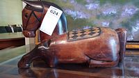 Full view of the horse wood carving in resting position showing geometric pattern on back and carved details on head and legs.