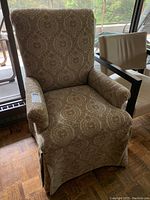 Front angled view of vintage high back upholstered armchair showing the fabric pattern and armrests.