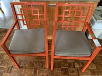 Pair of orange painted wood armchairs with gray cushions, showing geometric squared back design and surface wear.