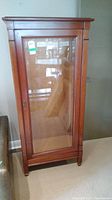 Front angled view of the tall wooden curio cabinet showing glass front door and wooden frame.