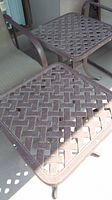 Two brown metal patio end tables with lattice design tops and curved legs.