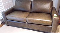 Front view of brown leather love seat with two seat cushions and two back cushions.