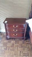 Full front view of dark wood night stand showing three drawers and carved side details.