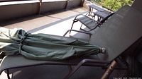 Patio lounger on a balcony or patio with green fabric umbrella or cover tied on top of seat area, metal frame visible with brown finish and mesh fabric seating.