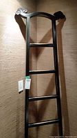 Full wood towel rack leaning in corner, showing full height and decorative scroll design on top ends