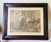 Framed etching artwork showing a group around a piano in an interior room.