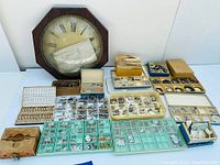 Overall view of wooden wall clock case and multiple trays and boxes of watch and clock parts