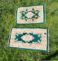 Two hunter green art deco patterned Chinese carpets placed on grass showing their full layout and color scheme.