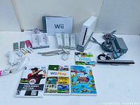 Full view of Nintendo Wii console bundle including the console, controllers, charging dock, sensor bar, power supply, AV cables, three Wii games, manuals, and additional accessories.