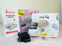 Sewing machine, instruction manual, power cord, bobbin accessories, and original box arranged for display